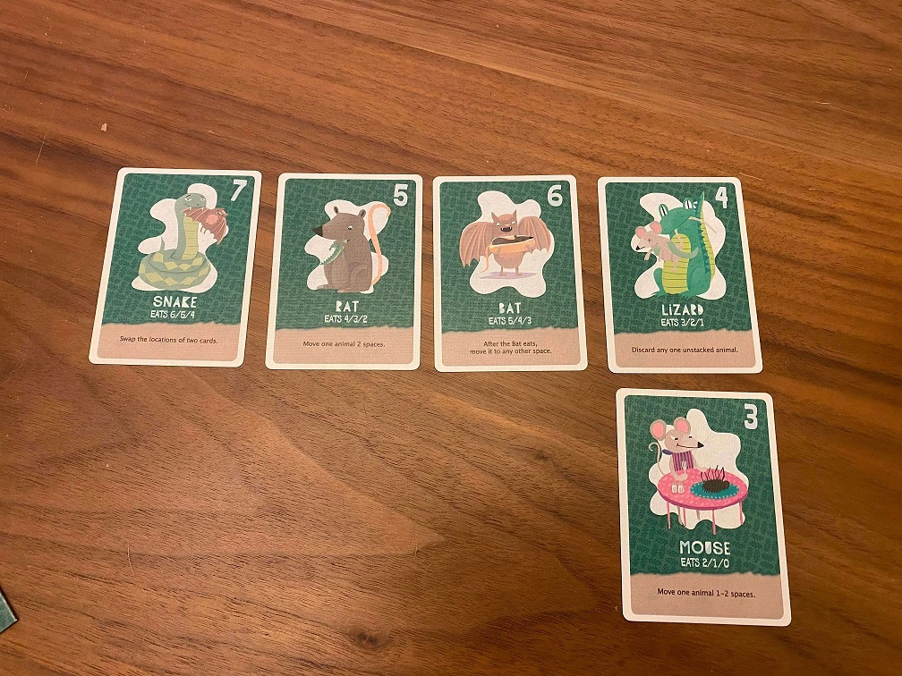 A "checker"s set up. Five land creatures are arranged in 2 rows with 4 cards on the top row, and 1 card on the bottom row to the far right. They are ordered 7, 6, 5, 4 on the top. 3 on the bottom.